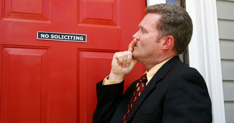 A man in suit and tie leaning against the door of a red building.