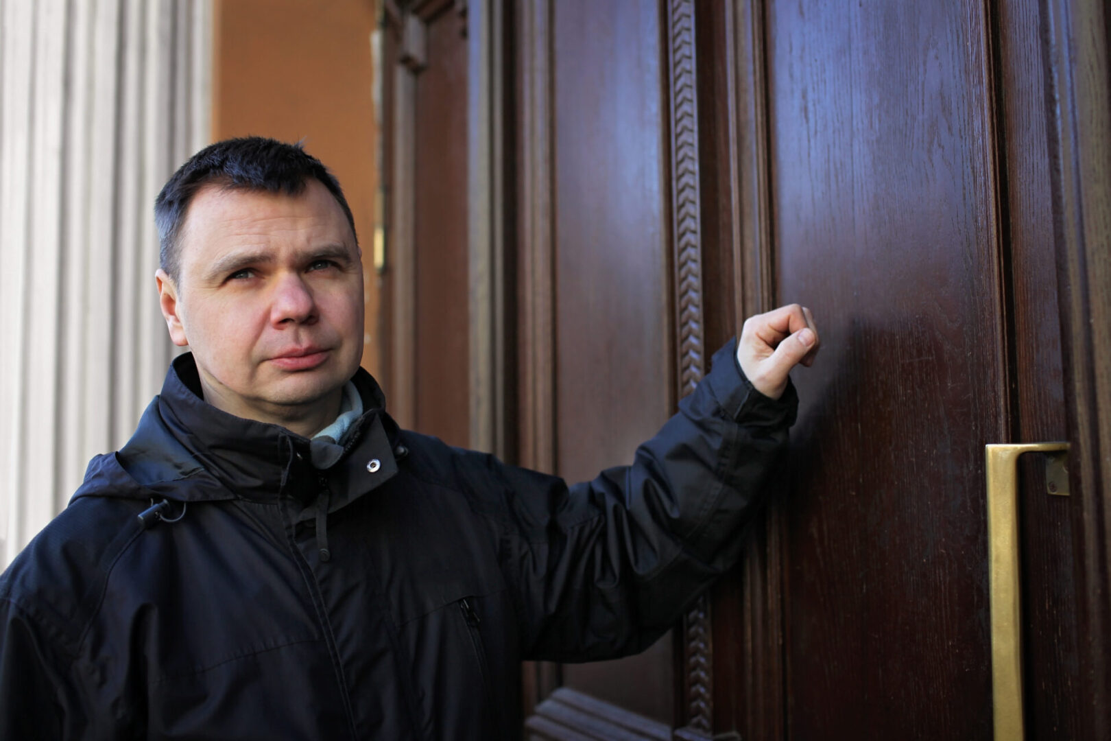 A man in black jacket holding on to door handle.