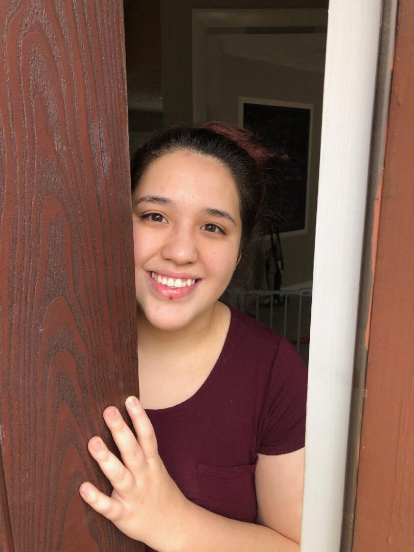 A girl smiling and peeking out from behind a door.